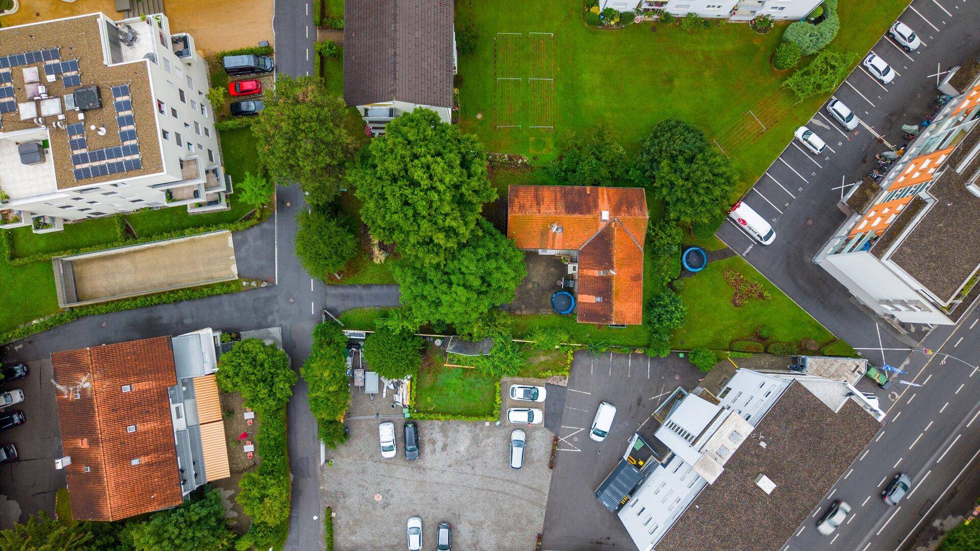Senkrechte Luftaufnahme eines Hauses mit rotem Dach, umgeben von Grünflächen und Parkplätzen.