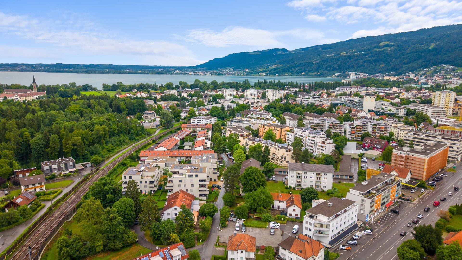 Panoramablick aus der Luft auf eine Stadt am See mit umliegenden Wäldern und Bergen in der Ferne.