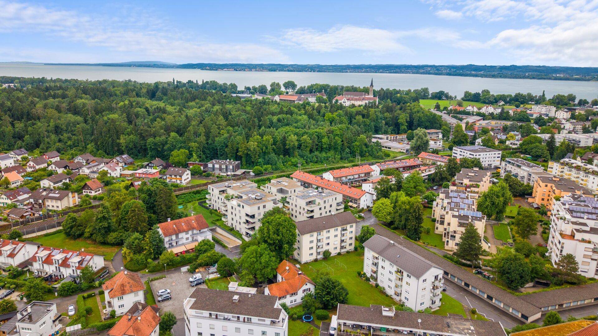 Weitläufige Luftaufnahme einer Stadtlandschaft mit großem See und ausgedehnten Waldgebieten im Hintergrund.