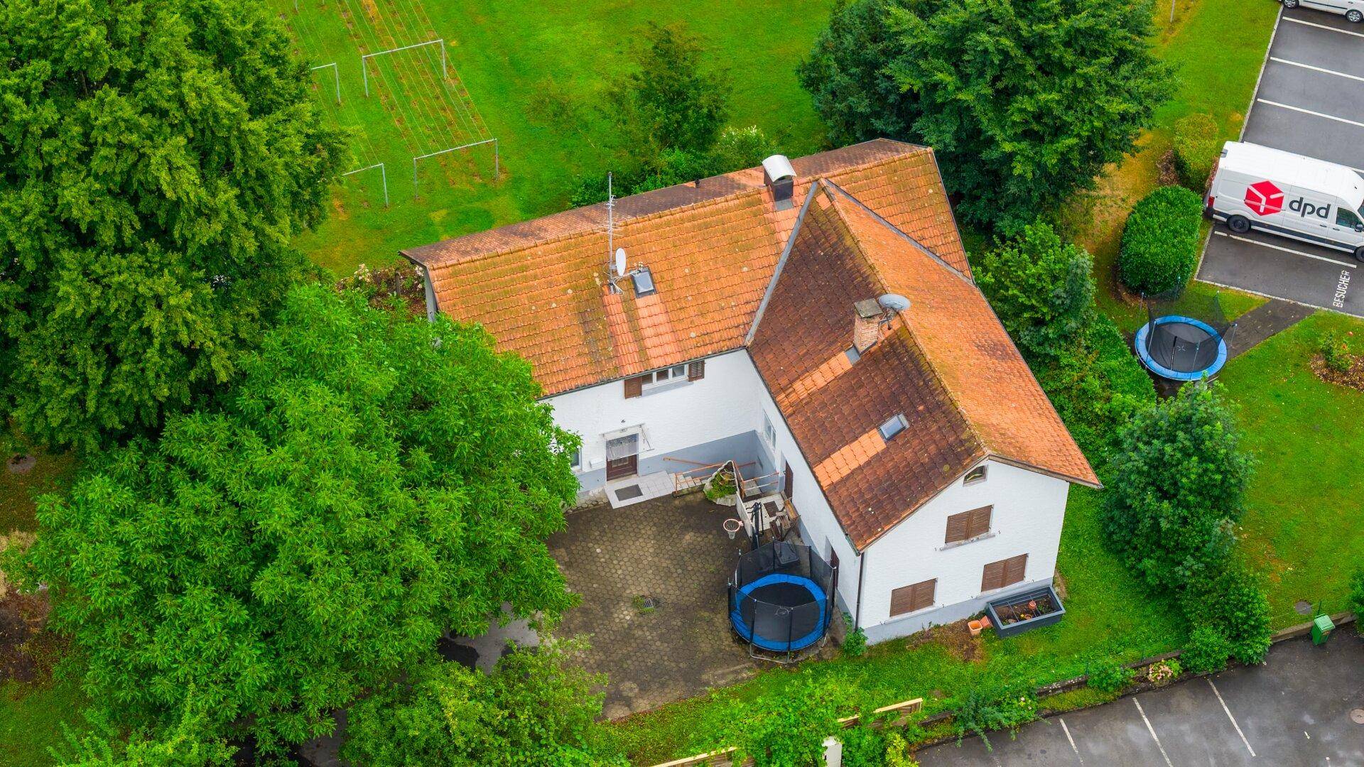 Detaillierte Luftaufnahme eines Hauses mit rotem Ziegeldach, Garten und Trampolin im Außenbereich.