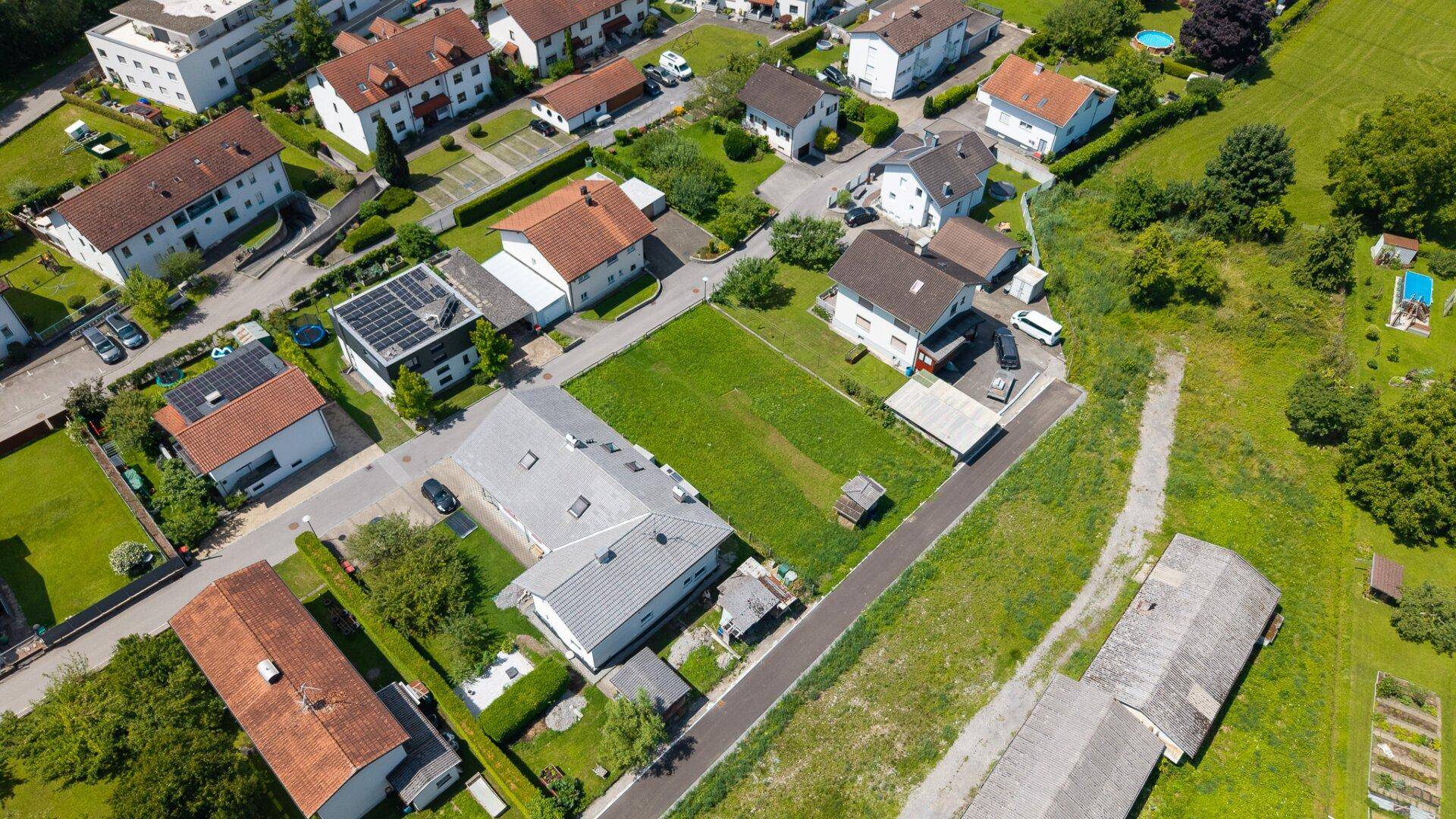 Nähere Luftaufnahme einer gepflegten Wohngegend mit Einfamilienhäusern, Gärten und viel Grünfläche.
