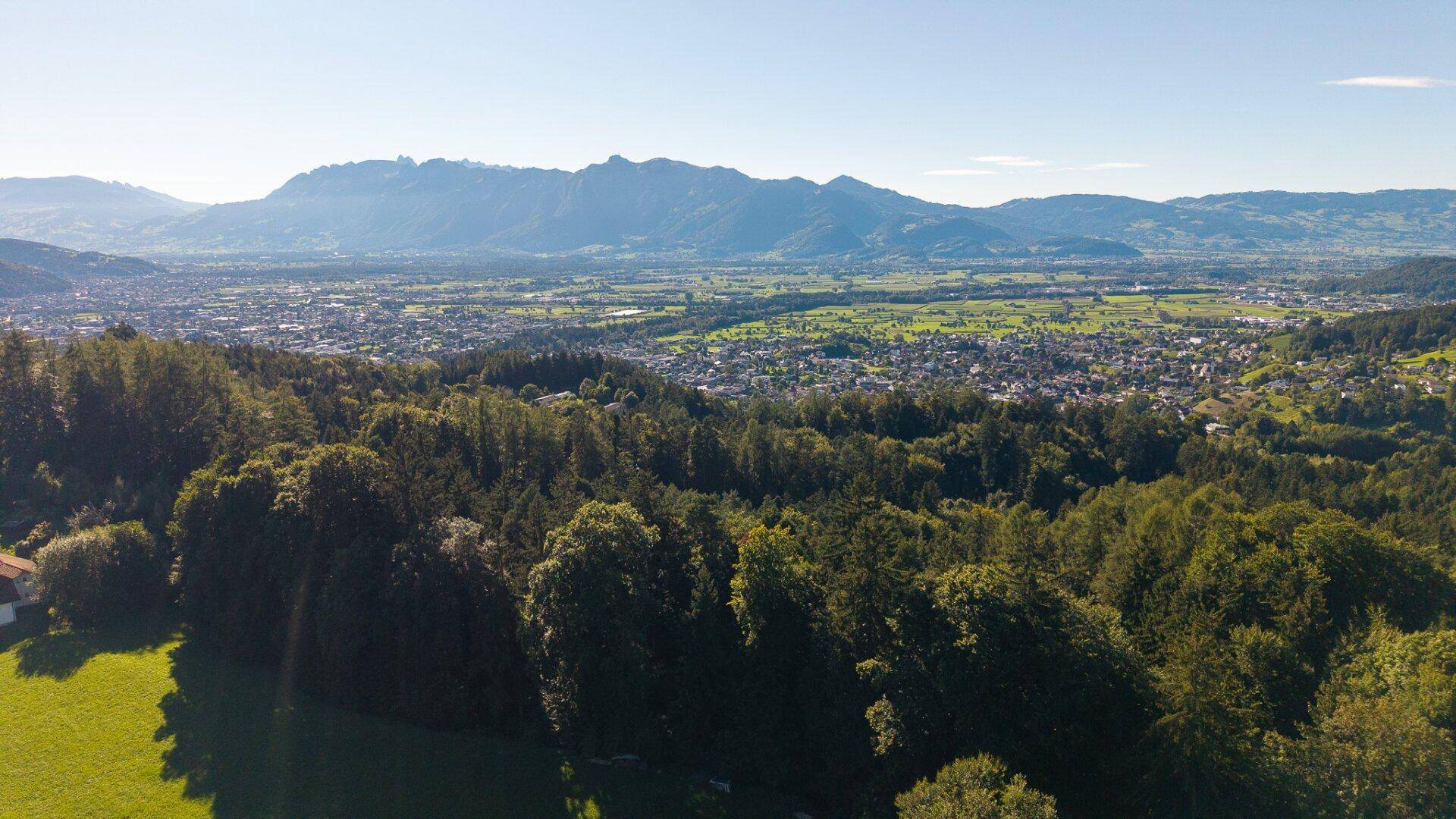 Weitläufiger Panoramablick von einem Hügel auf eine Stadt im Tal, umgeben von grünen Feldern.
