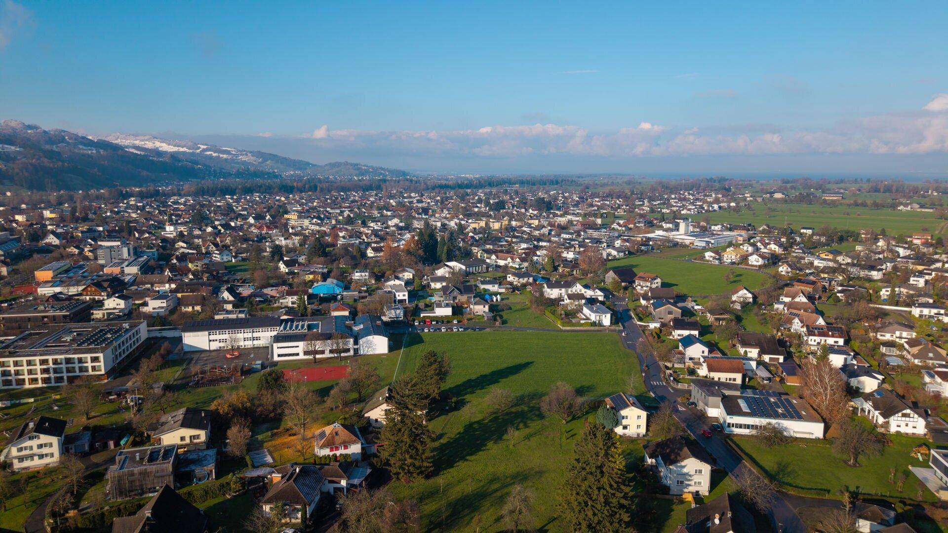 Weitläufige Luftaufnahme einer Wohnsiedlung mit angrenzenden Feldern und grüner Landschaft.