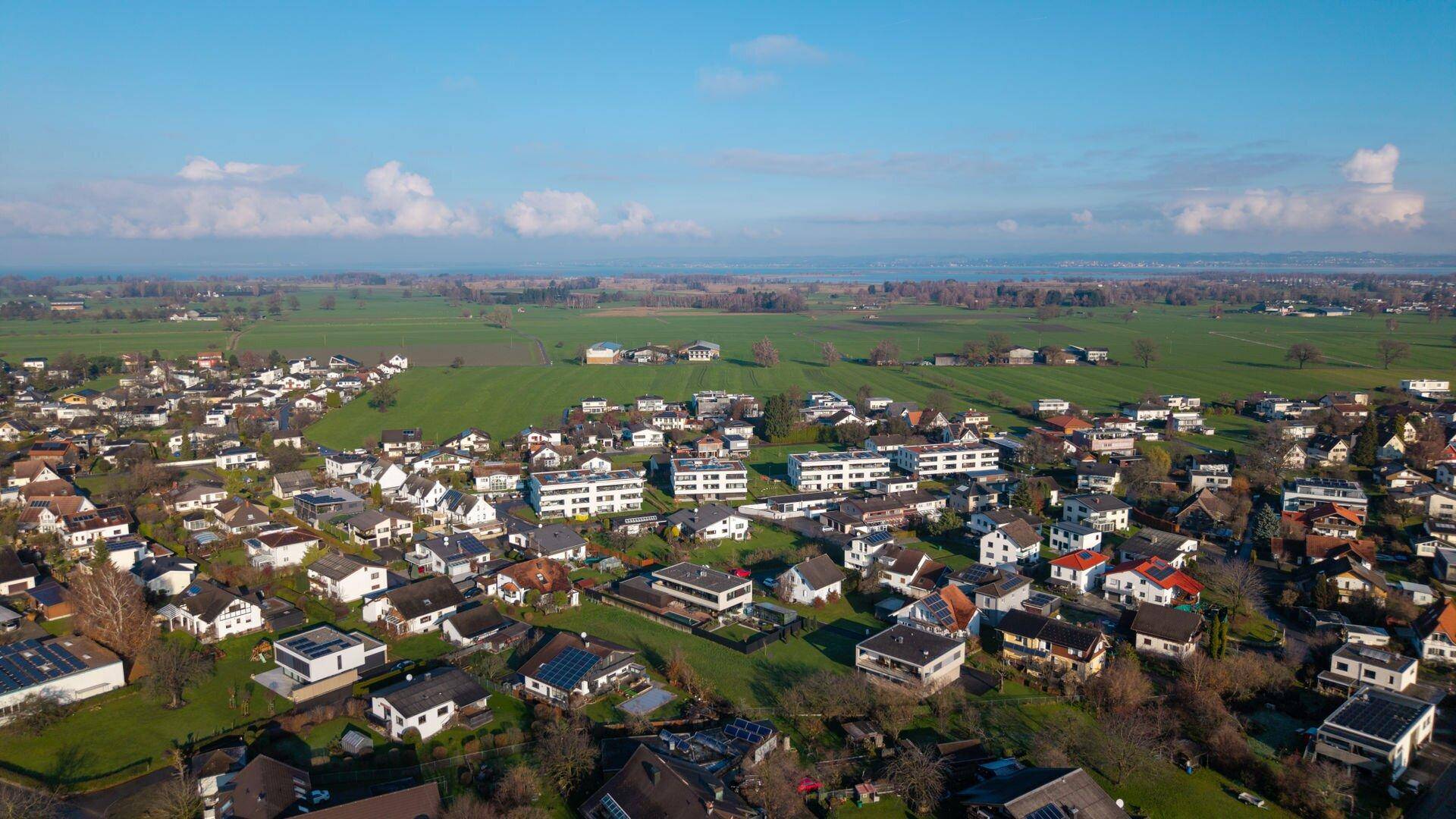 Luftaufnahme einer Wohngegend mit modernen Gebäuden, weiten Feldern und blauem Himmel.