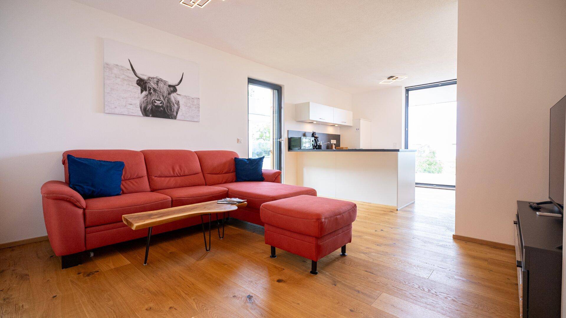 Geräumiges Wohnzimmer mit rotem Ecksofa, Holzboden und offener Verbindung zur Küche.