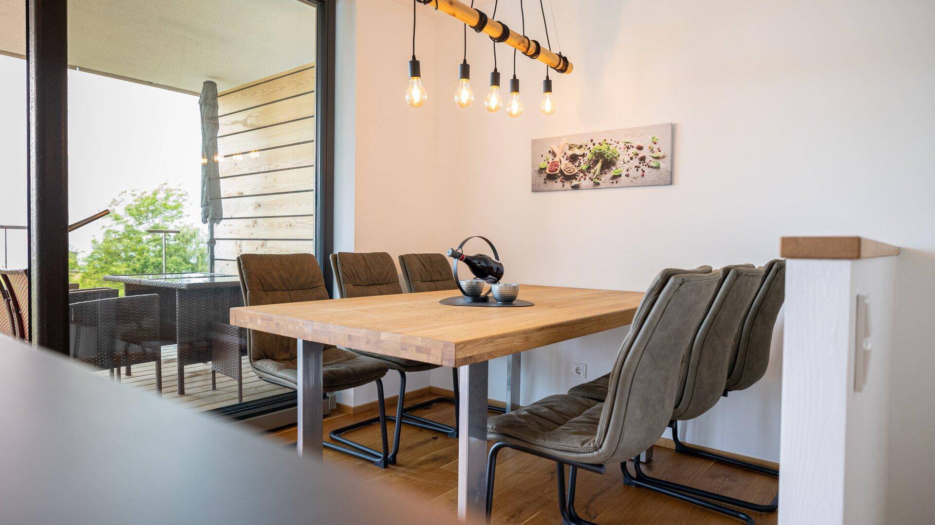 Essbereich mit Holztisch und moderner Beleuchtung, mit Zugang zur Außenterrasse.