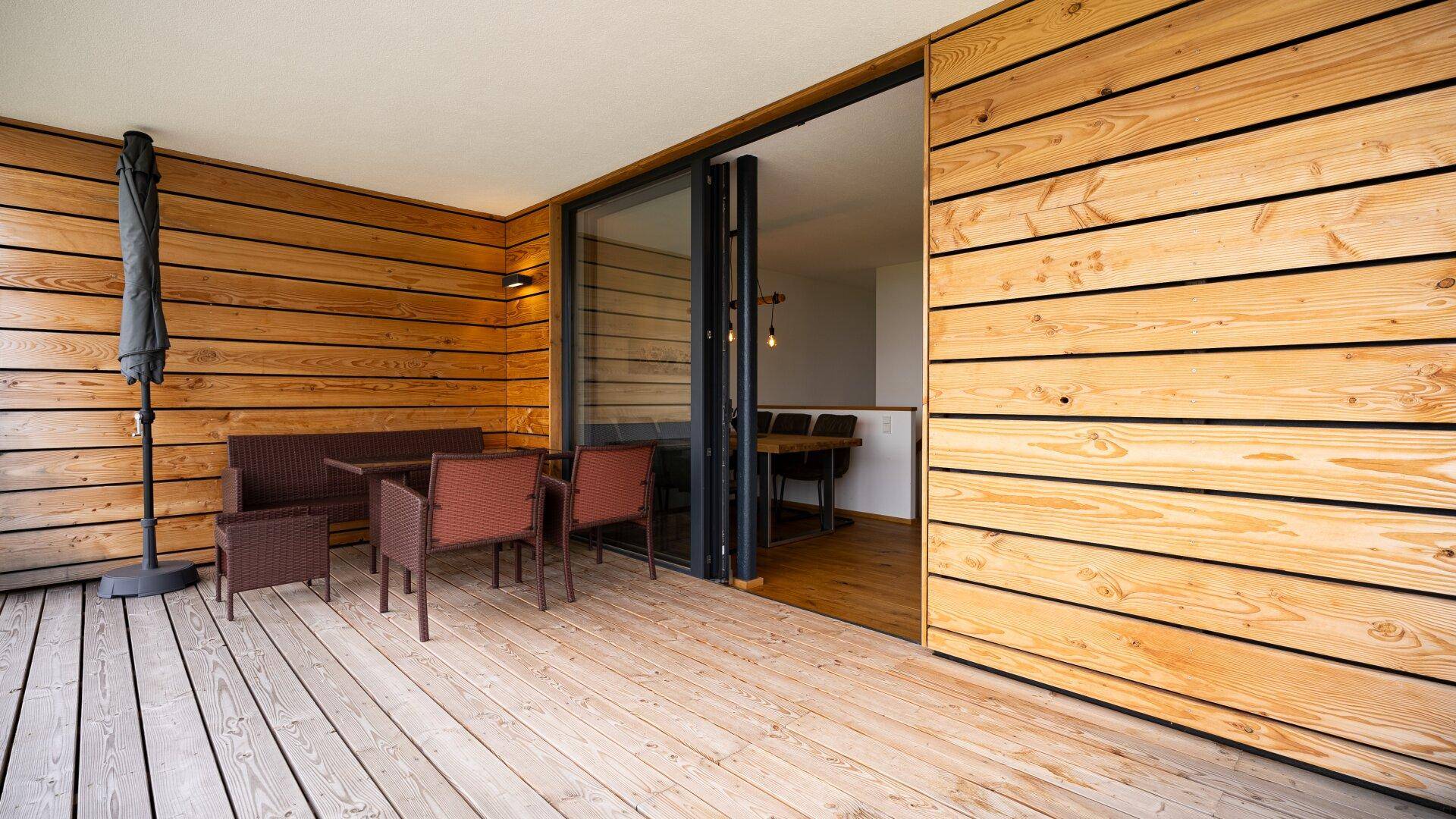 Geräumiger Balkon mit Holzverkleidung und Sitzgelegenheiten, direkt am Wohnbereich.