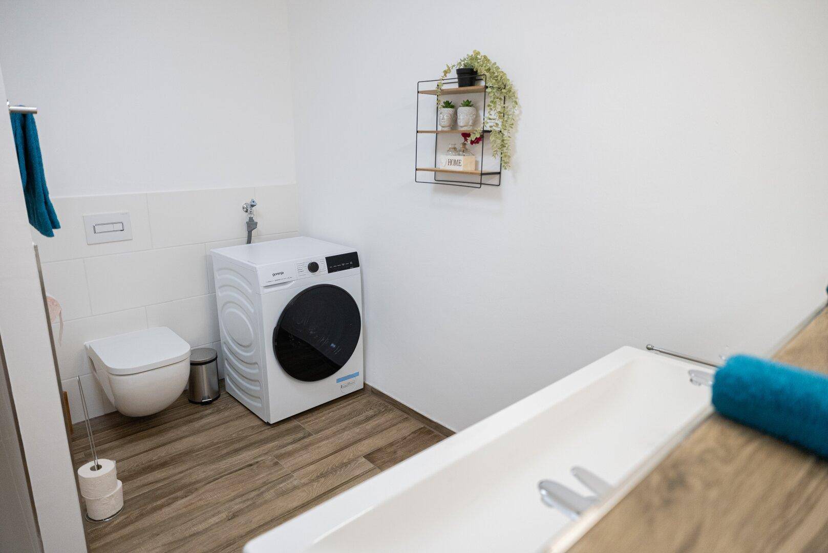 Modernes Badezimmer mit Waschmaschine, Toilette und Holzoptik-Boden.