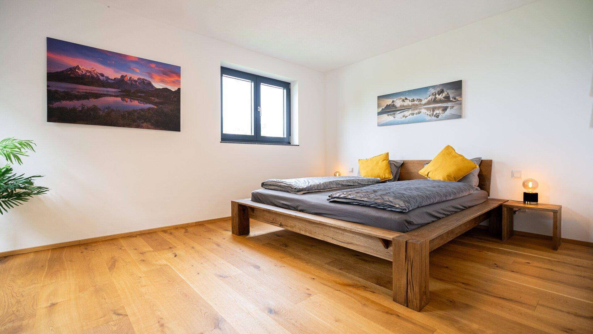 Helles Schlafzimmer mit Holzbett, Holzboden und großem Fenster.
