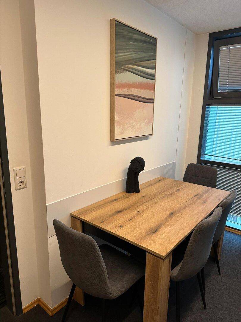 Essbereich mit Holztisch, modernen Stühlen und einem Kunstwerk an der Wand.