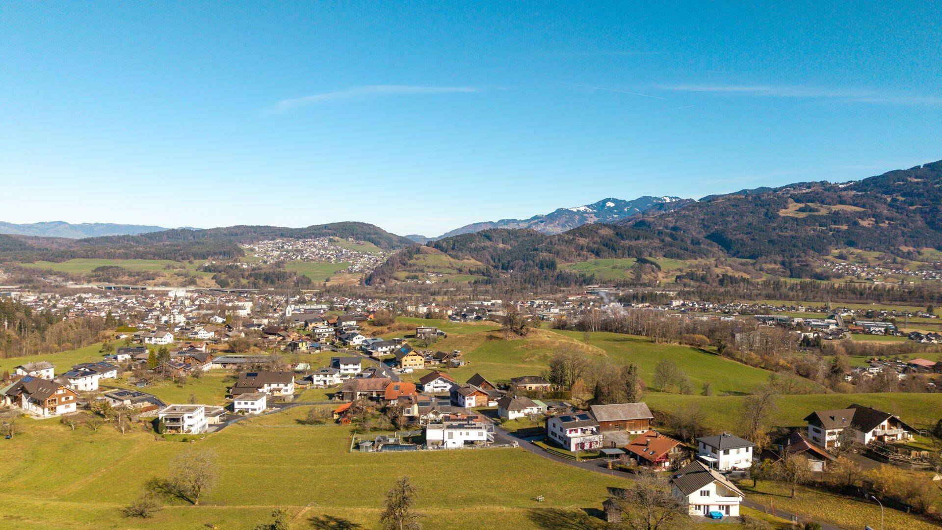 Luftaufnahme einer ausgedehnten Wohnsiedlung in einer grünen Hügellandschaft mit Fernblick auf die Umgebung.