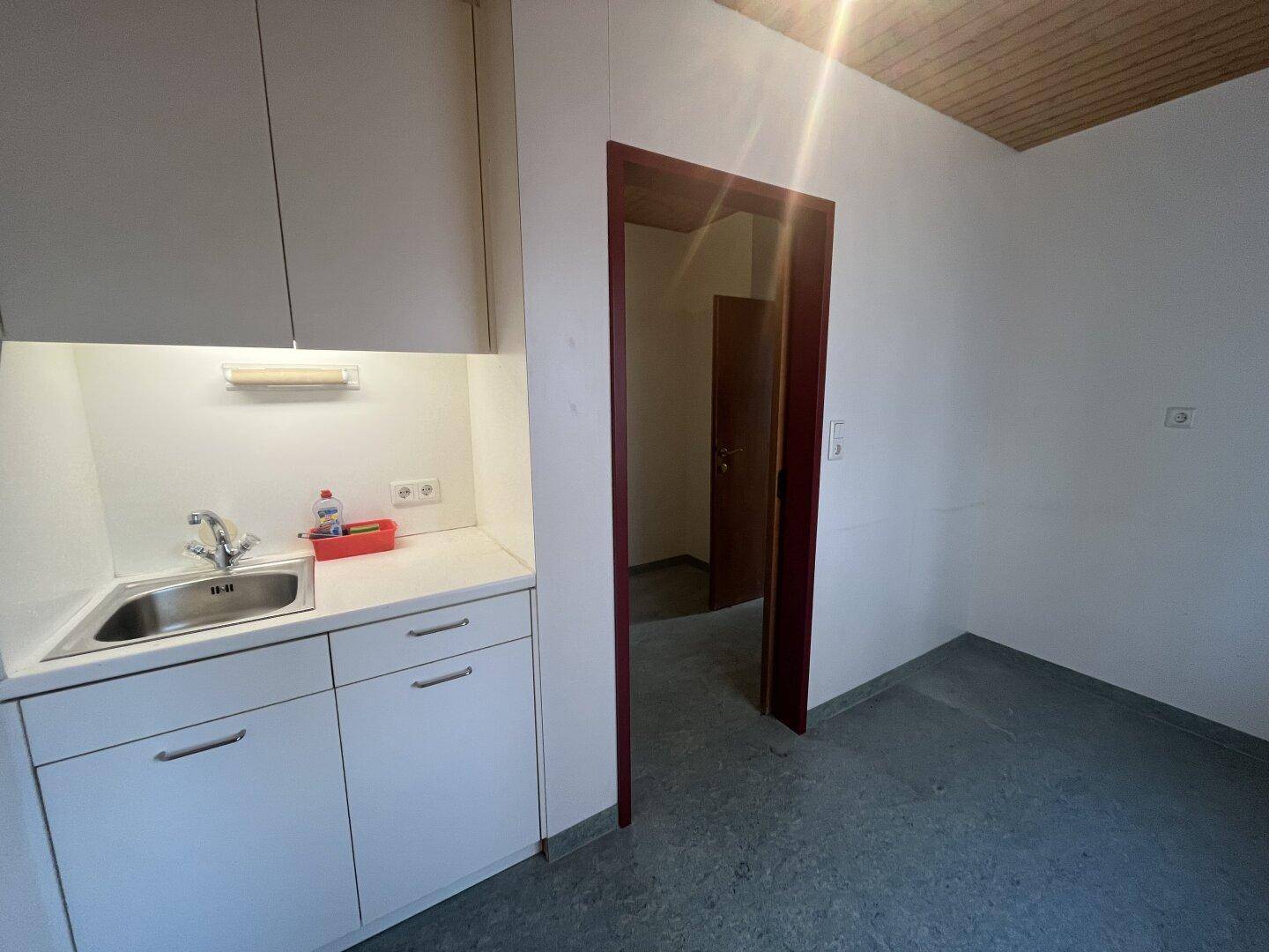 Kleine Teeküche mit weißen Schränken, Spülbecken und Arbeitsplatte, ideal für Pausenbereiche.