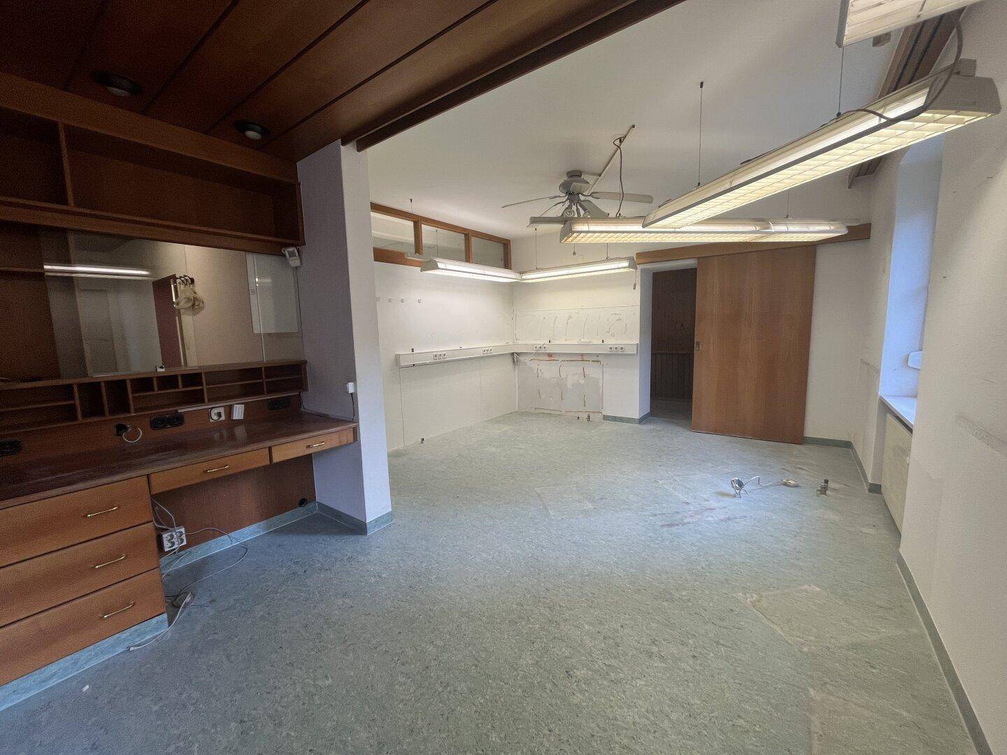 Geräumiger Büroraum mit Holzdecke, Einbauschreibtisch und Arbeitsflächen entlang der Wände.