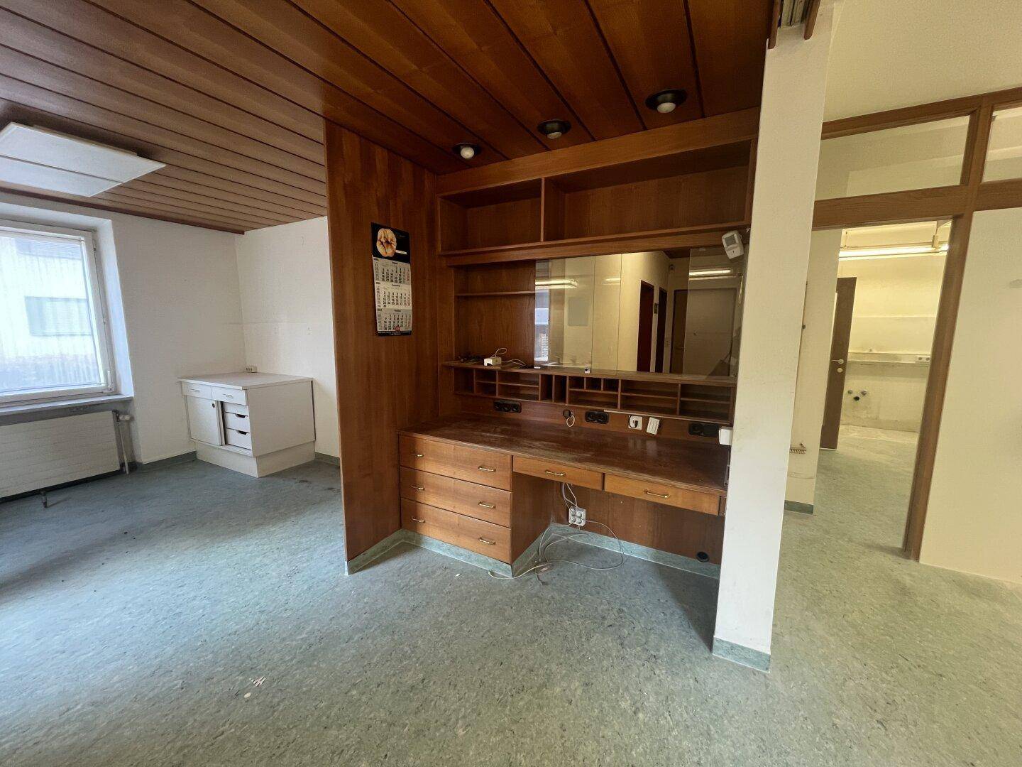 Geräumiger Büroraum mit integriertem Holzschreibtisch und Regalsystem, bietet viel Arbeitsfläche.