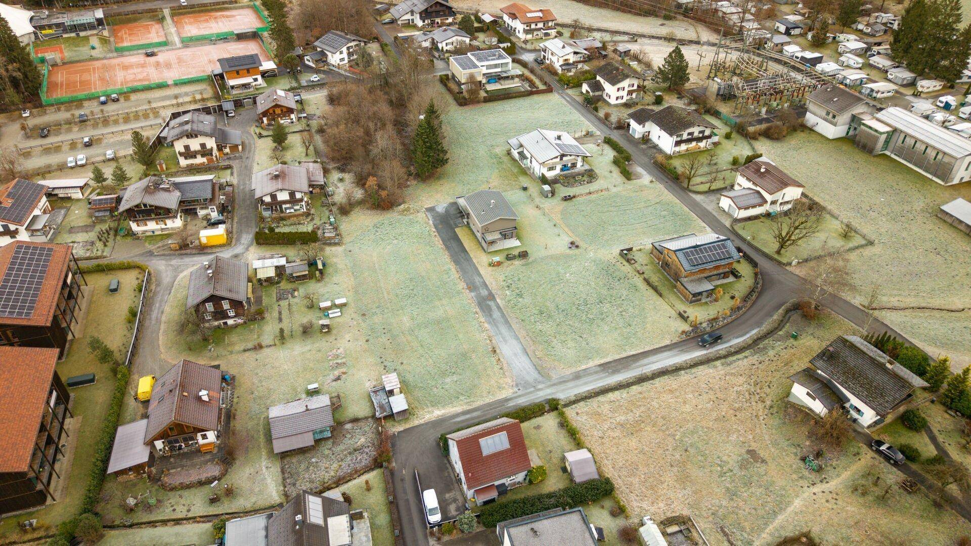 Luftaufnahme einer Wohnsiedlung mit Häusern und frostbedeckten Grundstücken, angrenzend an Tennisplätze.