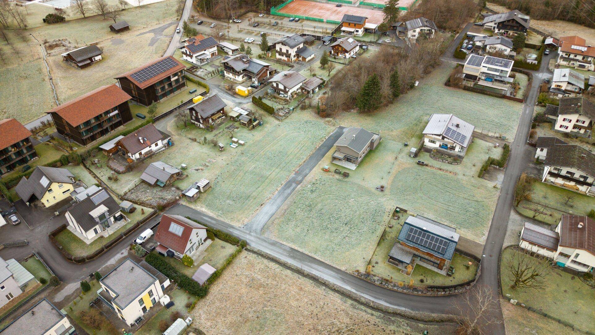 Überblick aus der Luft über eine Wohngegend mit Häusern, frostigen Wiesen und roten Tennisplätzen im Vordergrund.