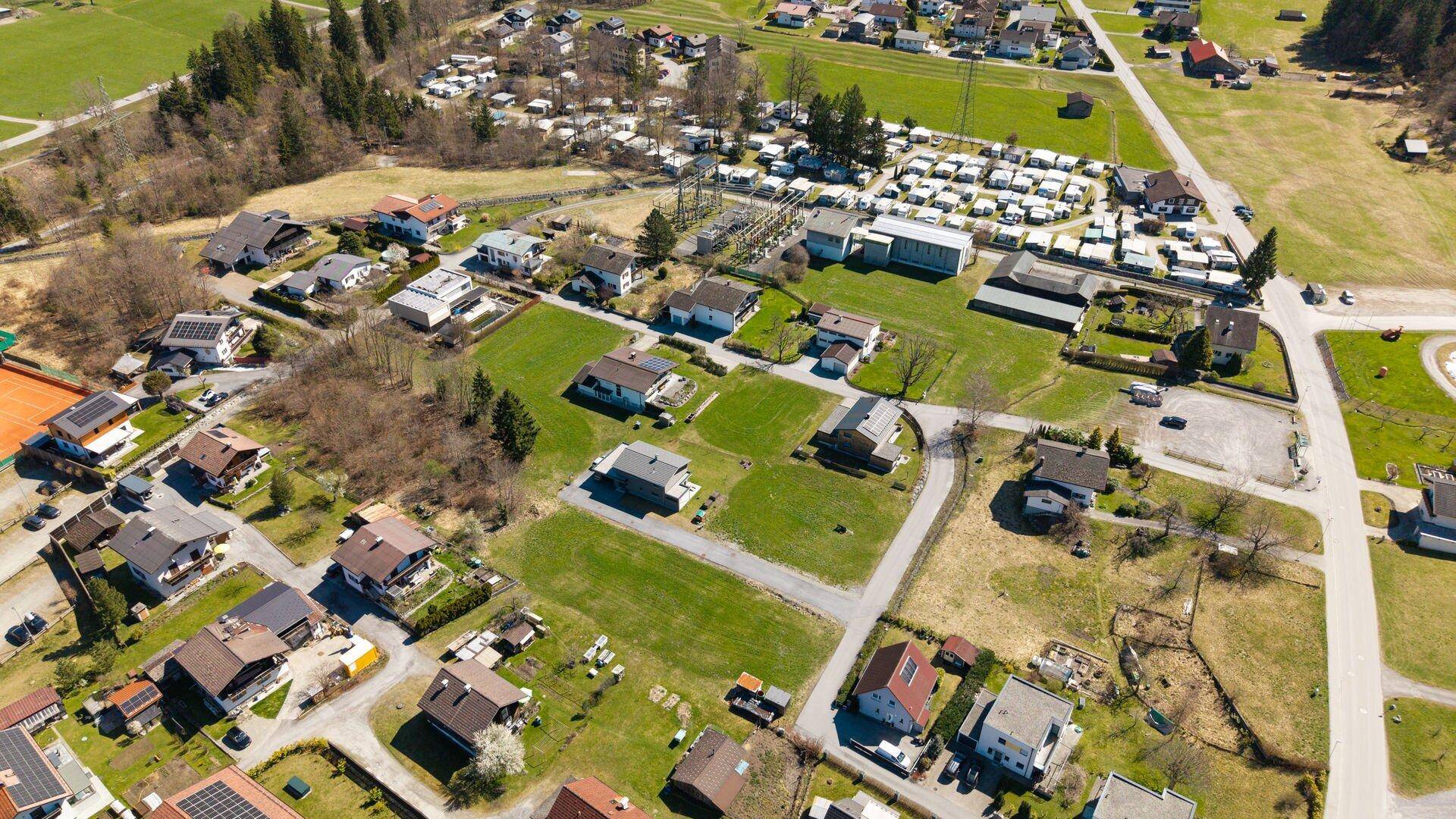 Luftaufnahme einer Wohngegend mit verschiedenen Häusern, grünen Gärten und einem großen Campingbereich.