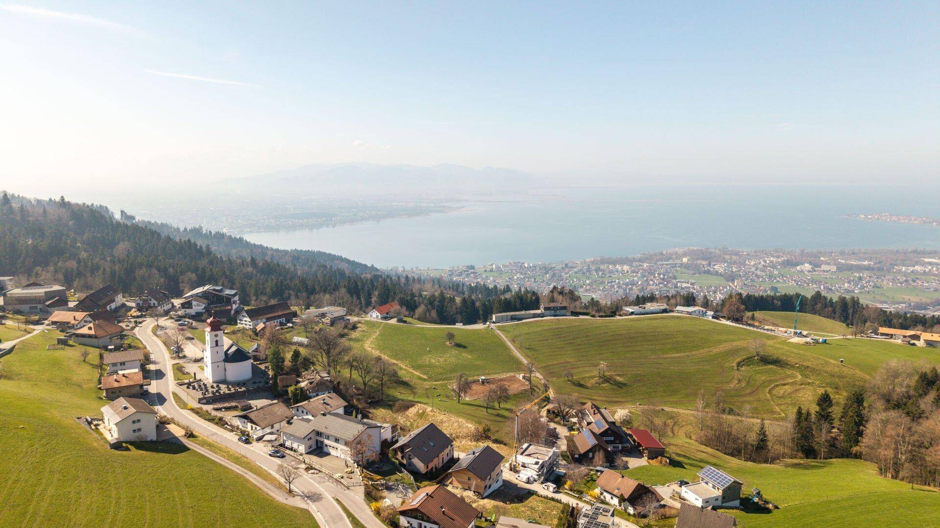 Panoramische Luftaufnahme eines Dorfes mit Häusern und einem großen See im Hintergrund.