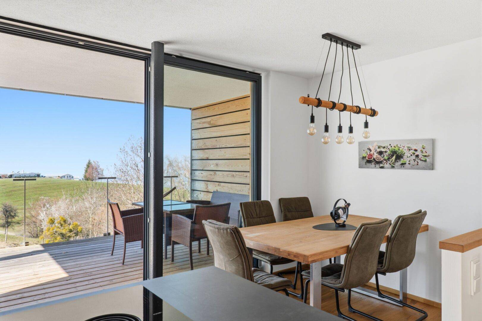Essbereich mit Holztisch, modernen Stühlen und großem Schiebefenster zum Balkon.