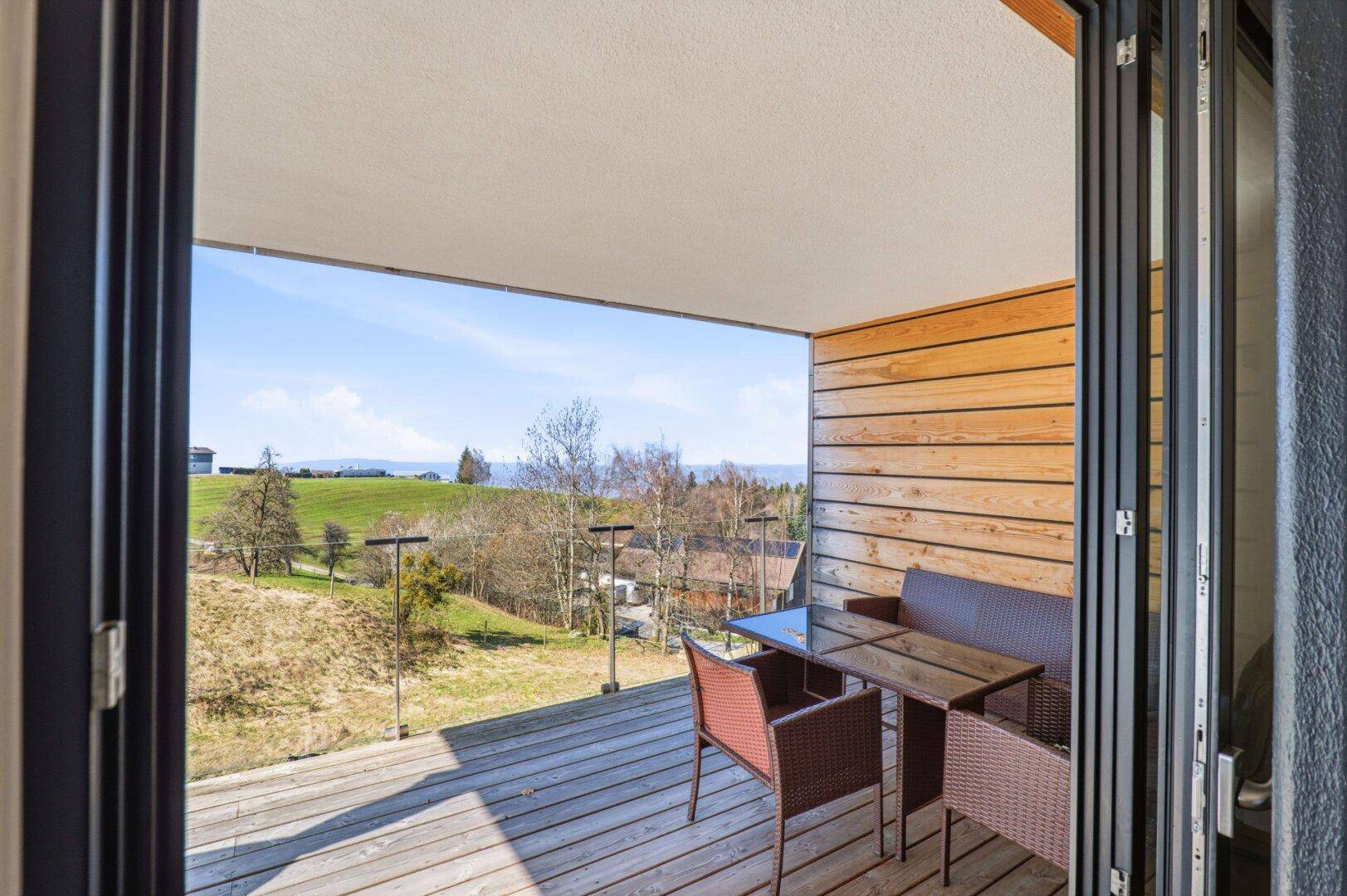 Geräumiger Balkon mit Holzbelag, Sitzmöbeln und weitem Blick auf die grüne Landschaft.
