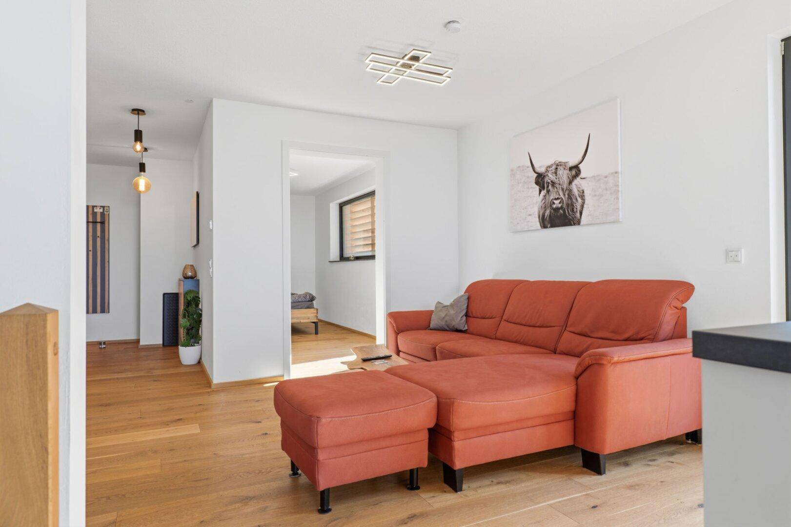 Gemütlicher Wohnbereich mit rotem Ecksofa, Holzboden und moderner Deckenleuchte.