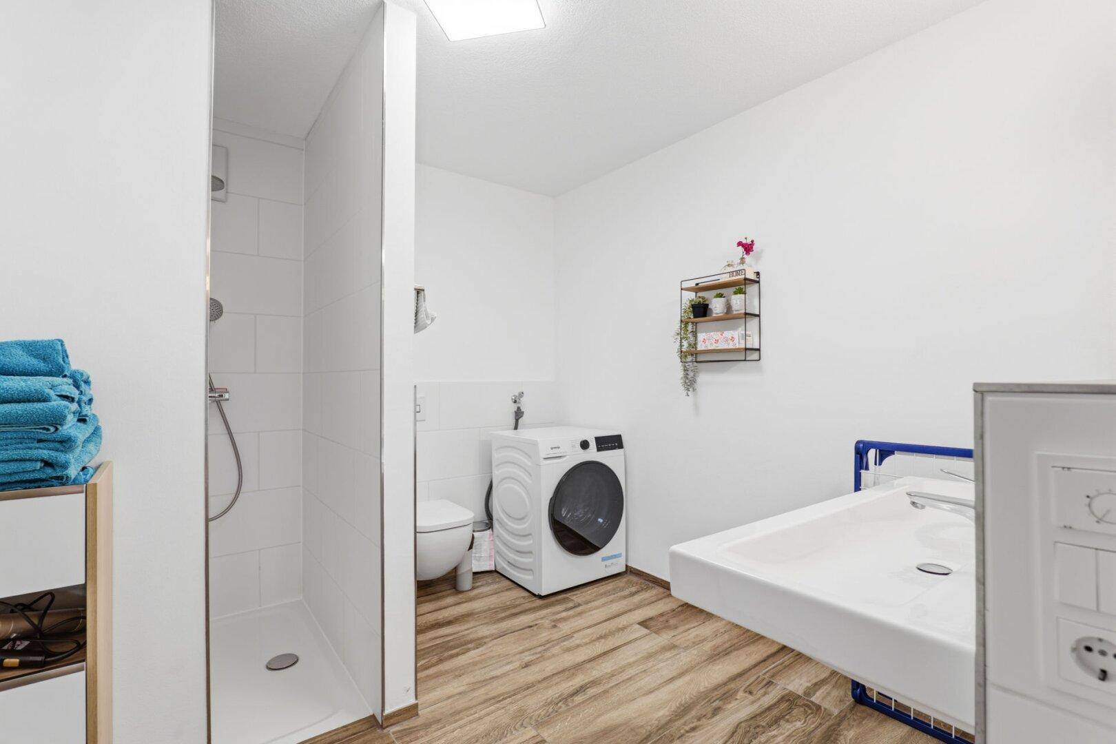 Praktischer Hauswirtschaftsraum mit Dusche, Toilette und Waschmaschine.