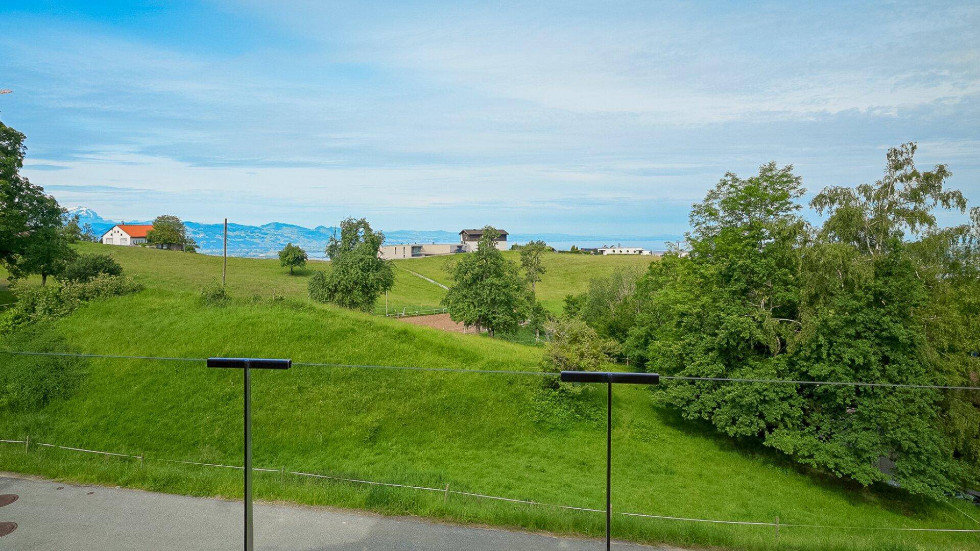 Panoramablick auf grüne Hügel und einen See in der Ferne, gesehen von einem Balkon.