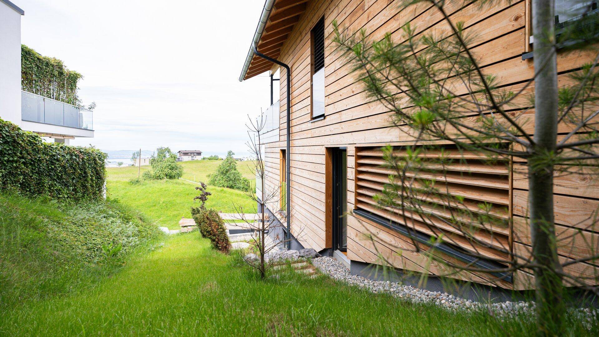 Moderne Holzfassade des Hauses mit grünem Garten und weitem Blick auf den See.