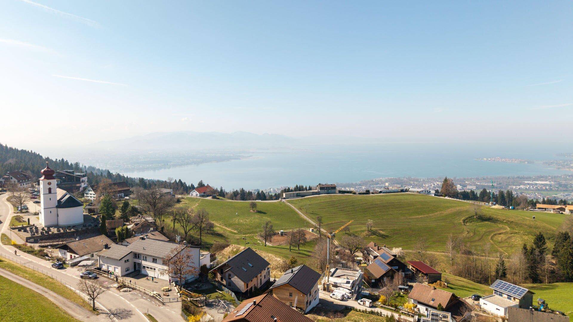 Weitläufiger Blick auf ein malerisches Dorf mit Kirche, See und Berglandschaft.