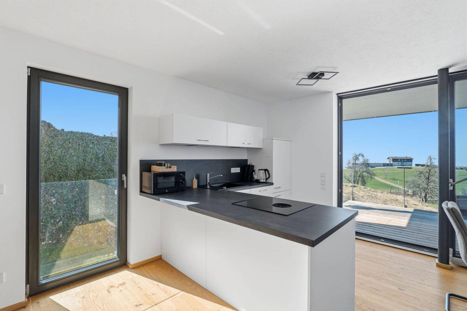 Offene Küche mit weißen Fronten und großzügigem Zugang zu einer Terrasse mit Weitblick.
