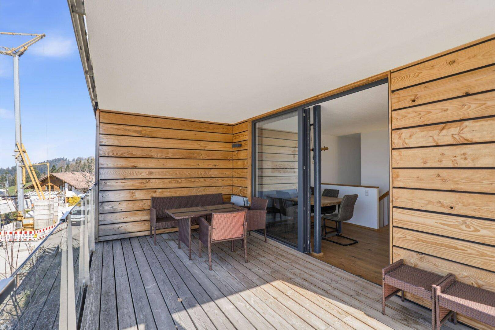 Große Holzterrasse mit Glasgeländer und Sitzmöbeln, angrenzend an ein modernes Gebäude.