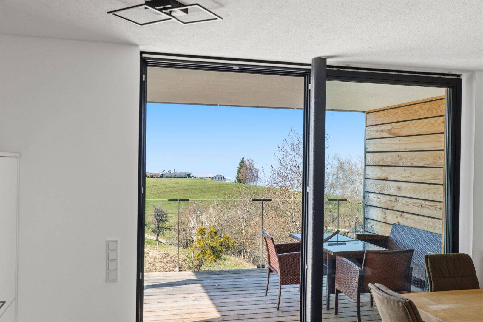 Heller Essbereich mit Blick durch große Fenster auf eine Terrasse und die umliegende Landschaft.