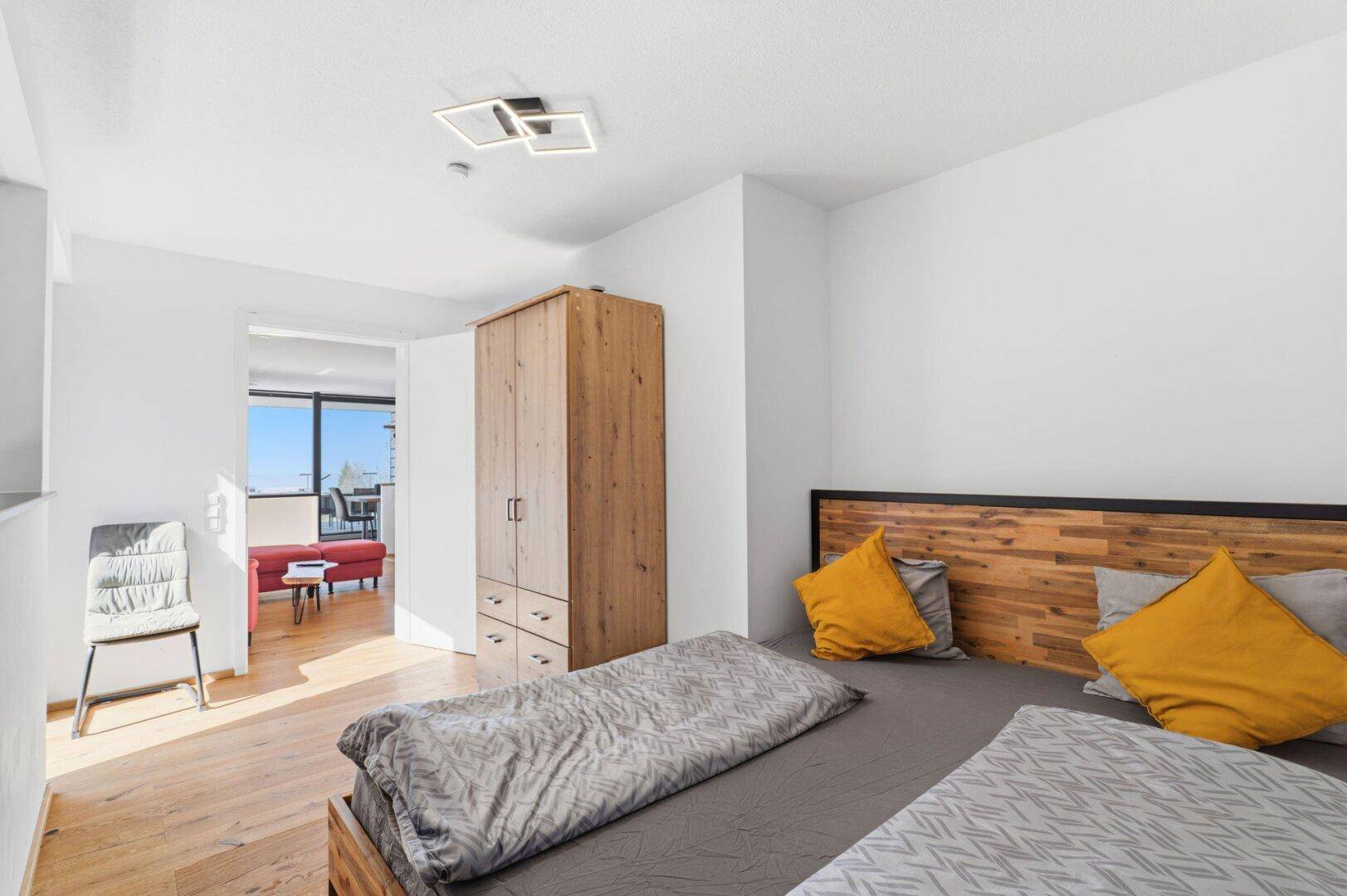 Helles Schlafzimmer mit Holzbett, Kleiderschrank und Blick auf den Wohnbereich und die Landschaft.