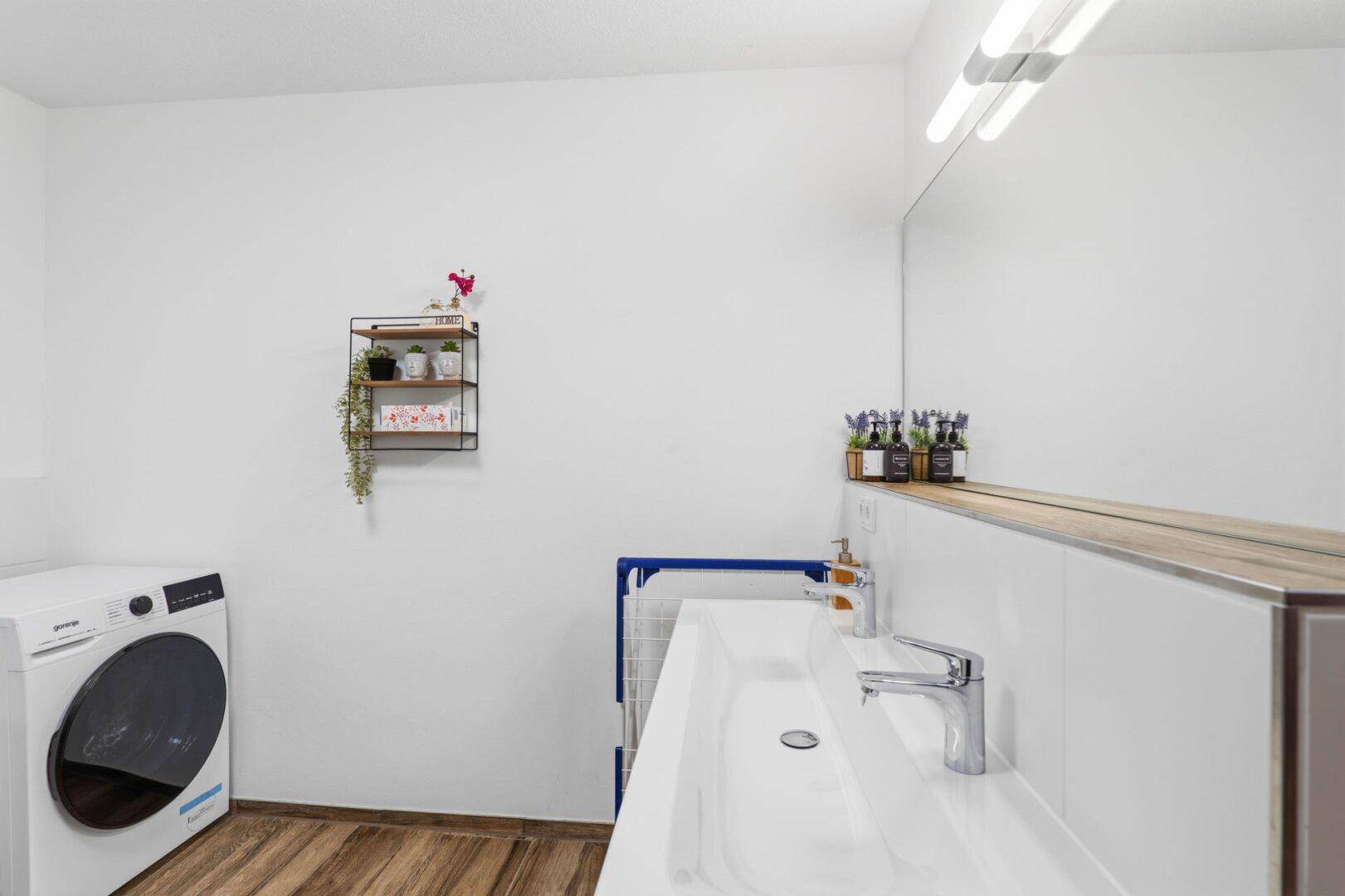 Modernes Badezimmer mit Doppelwaschbecken, Waschmaschine und großem Spiegel.