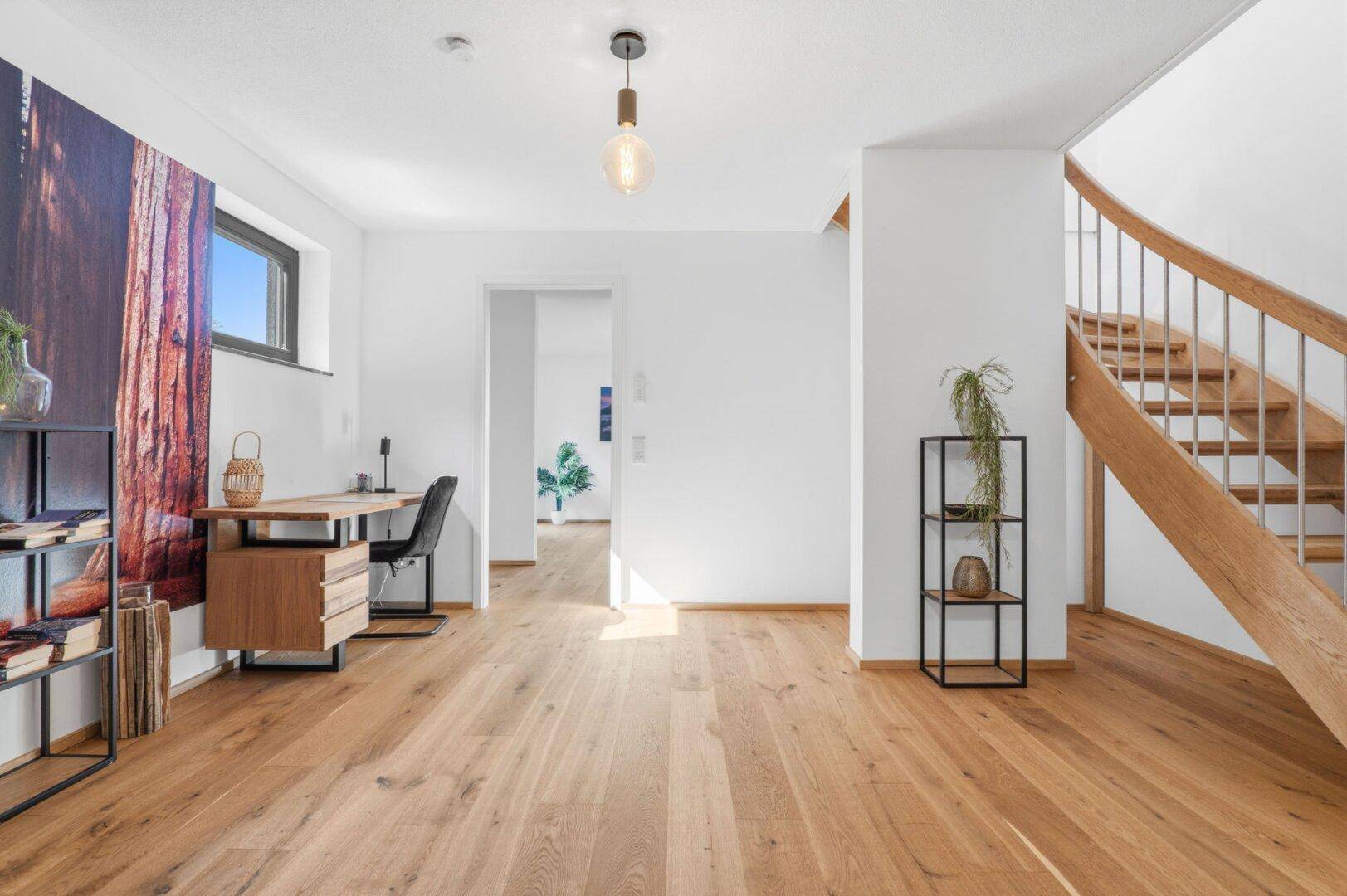Heller Flur mit Holztreppe, Schreibtisch und großflächiger Wanddekoration.