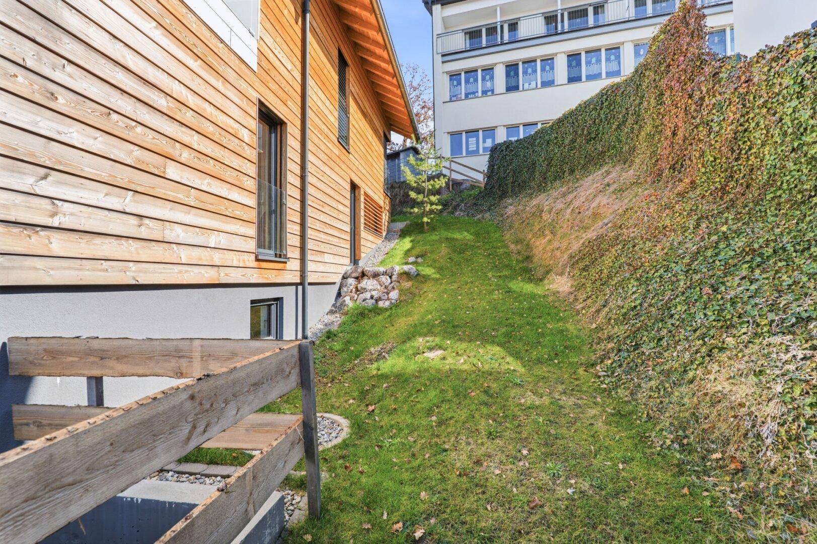 Holzfassade eines Gebäudes mit grünem Hang und Blick auf die Umgebung.