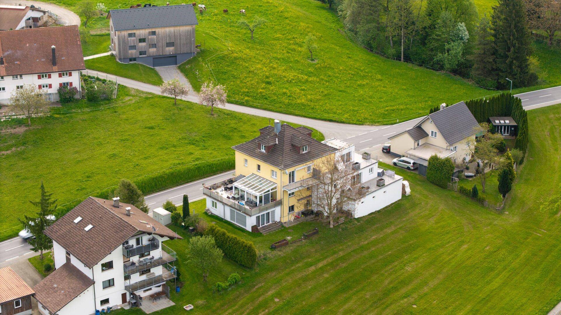 Luftaufnahme eines Wohnhauses mit Wintergarten und umliegenden grünen Wiesen.