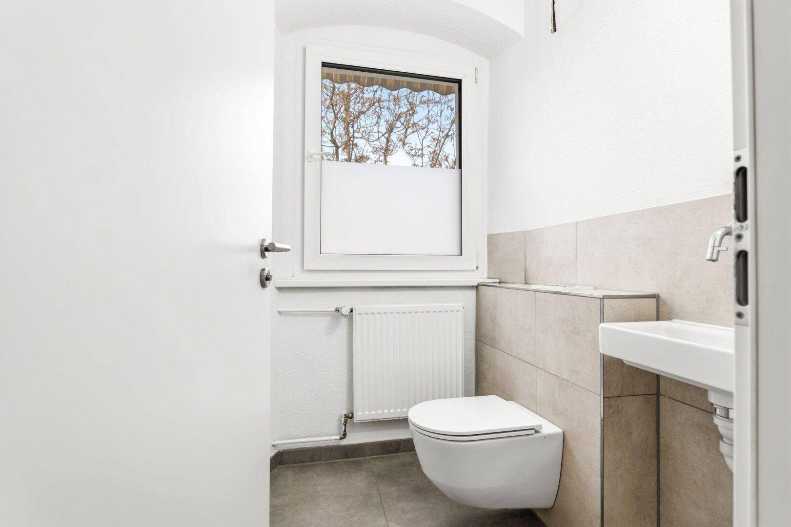 Modernes Gäste-WC mit wandhängender Toilette, kleinem Waschbecken und Fenster.
