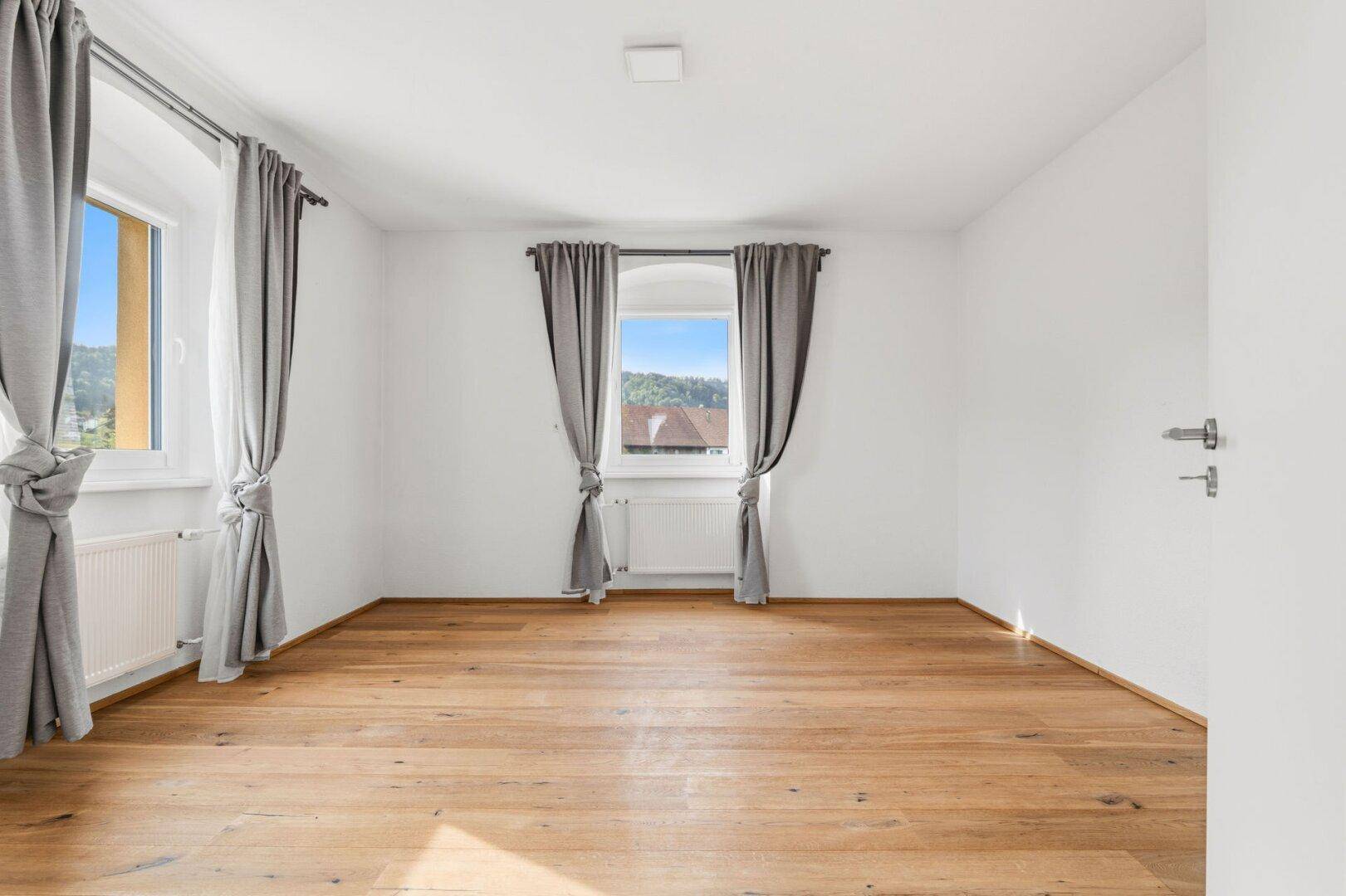 Großes Schlafzimmer mit Holzdielenboden, hellen Wänden und mehreren Fenstern für viel Licht.