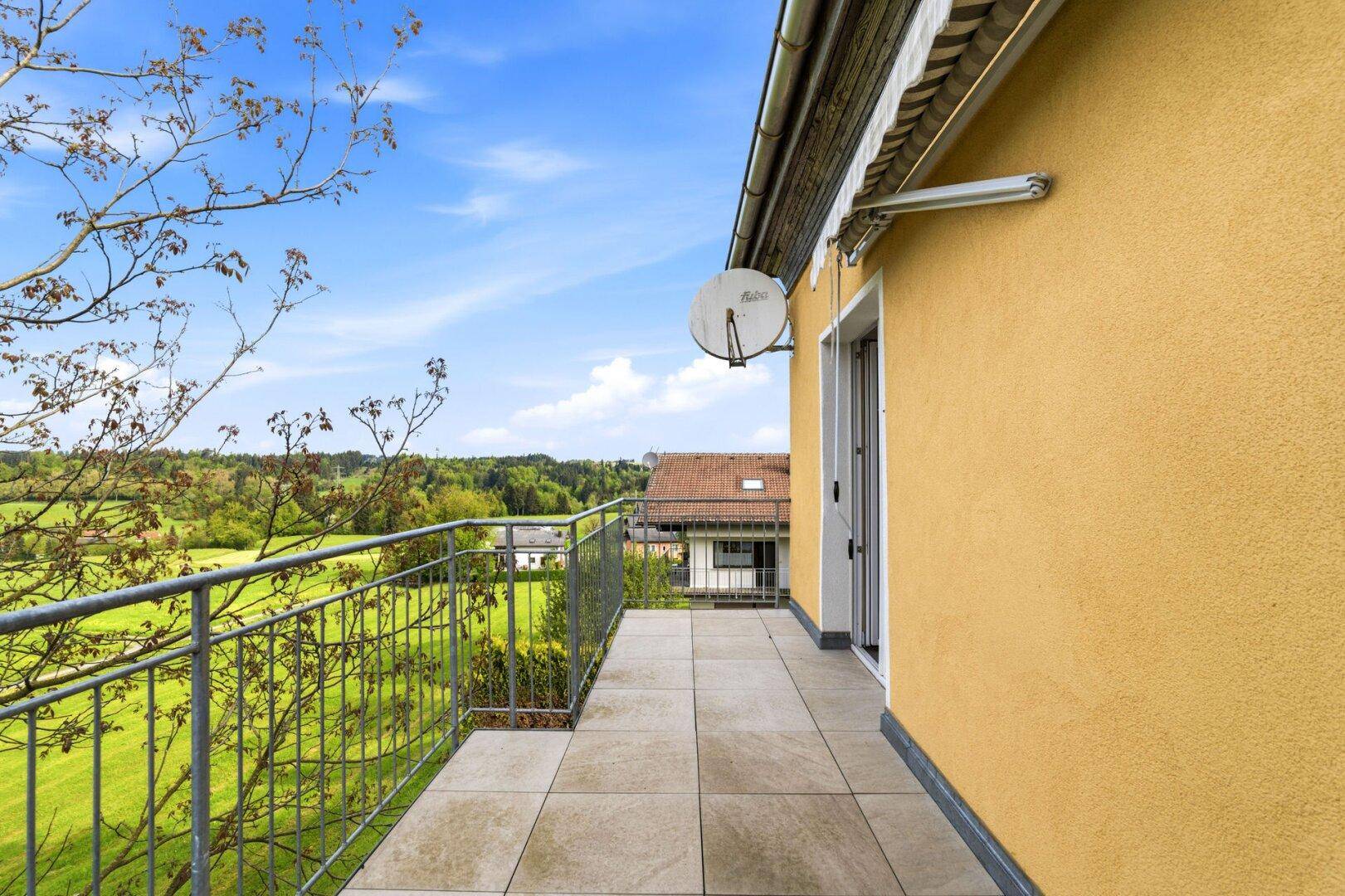 Langer Balkon mit Fliesenboden, gelber Fassade und weitem Blick in die Natur.