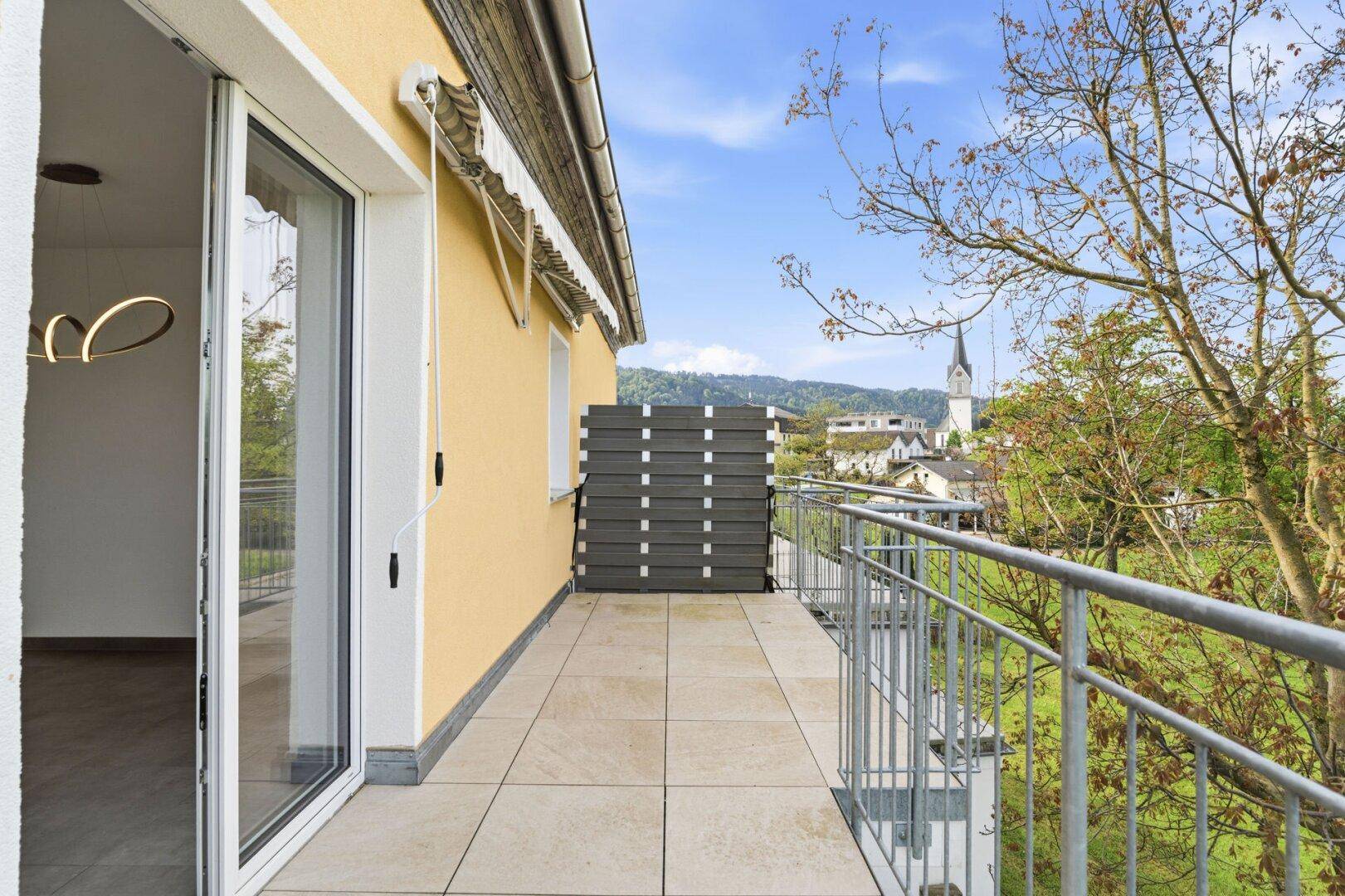 Geräumiger Balkon mit Fliesenboden und Blick auf die umliegende Ortschaft und Landschaft.