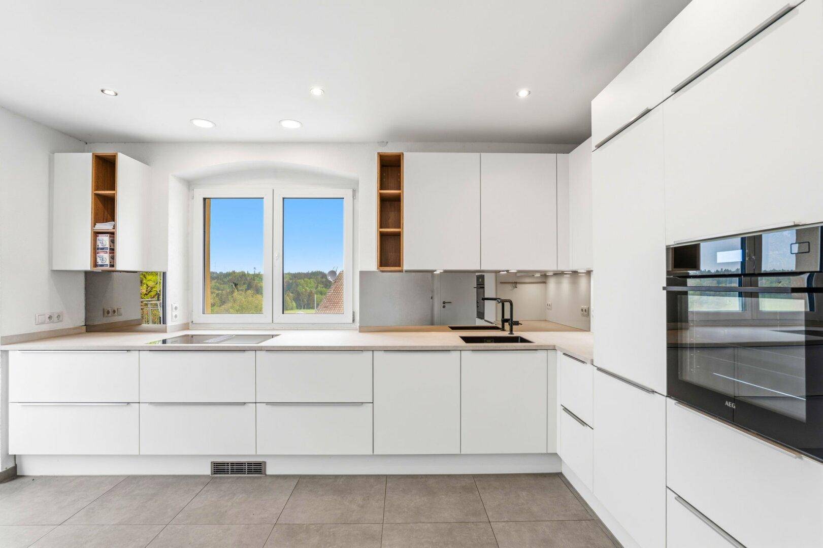 Moderne Einbauküche mit weißen Fronten, integriertem Backofen und Blick ins Grüne.