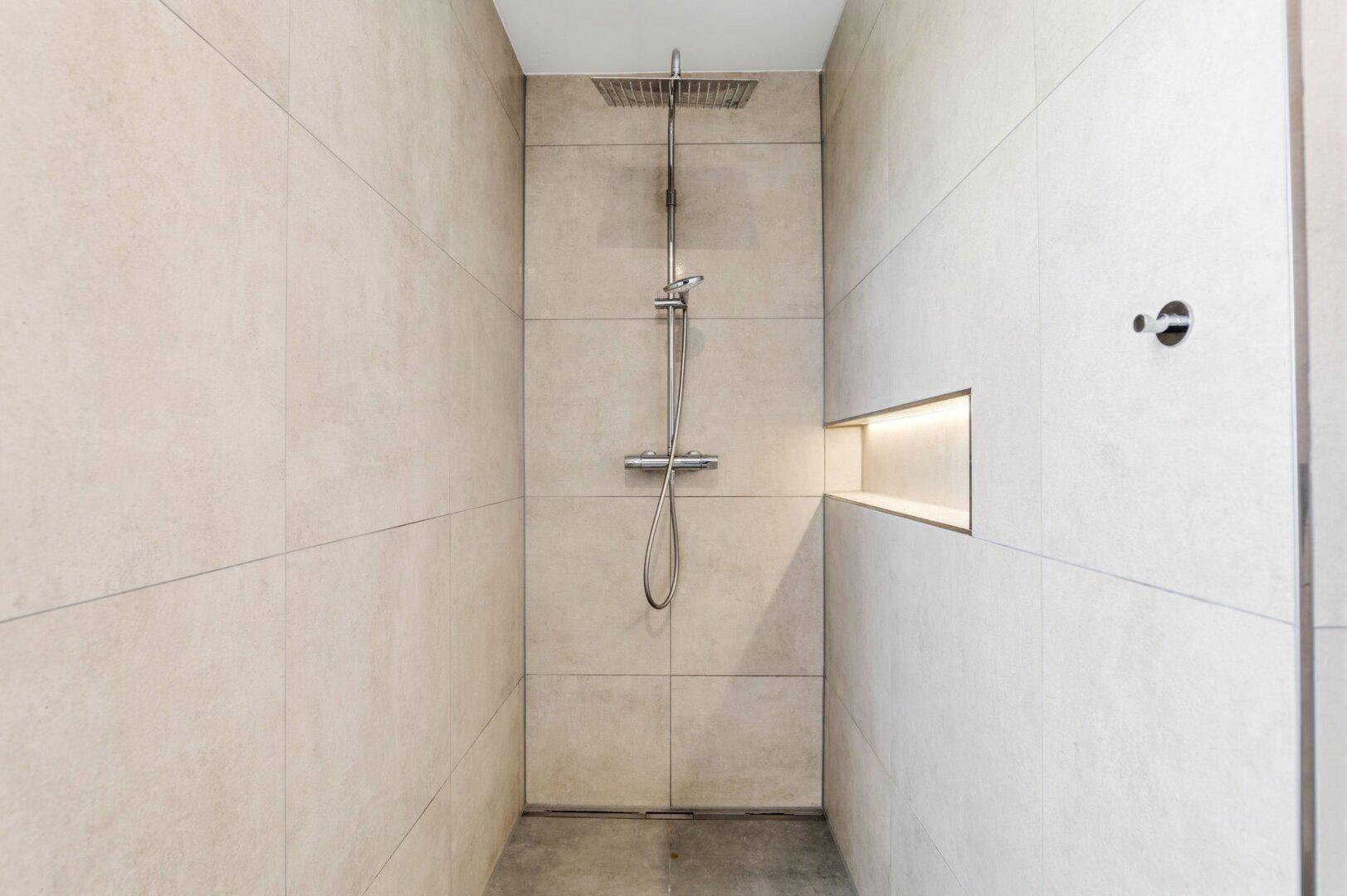 Moderne begehbare Dusche mit Regenduschkopf und integrierter Nische in beigefarbenen Fliesen.