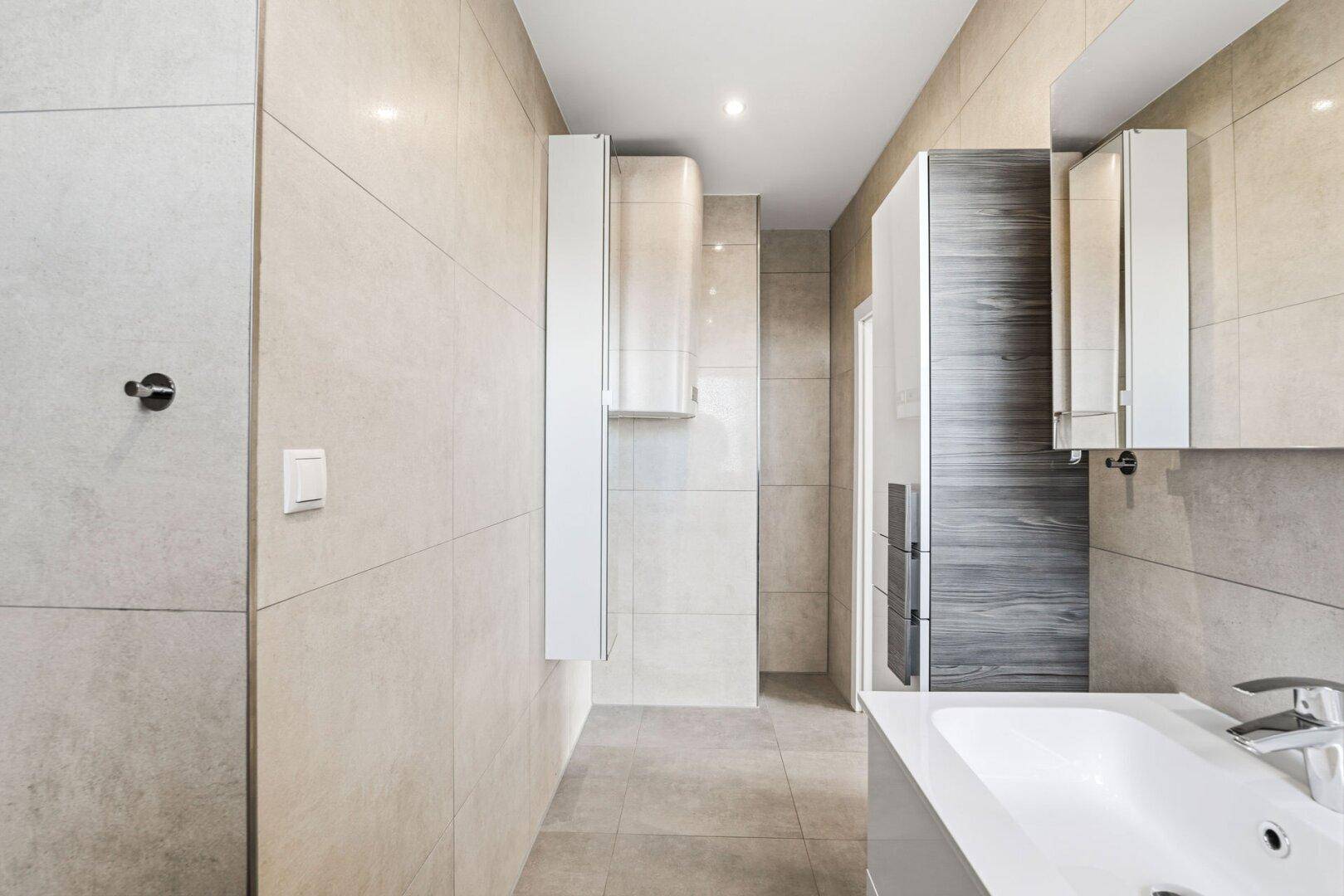 Modernes Badezimmer mit beigefarbenen Fliesen, Einbauschränken und minimalistischem Design.