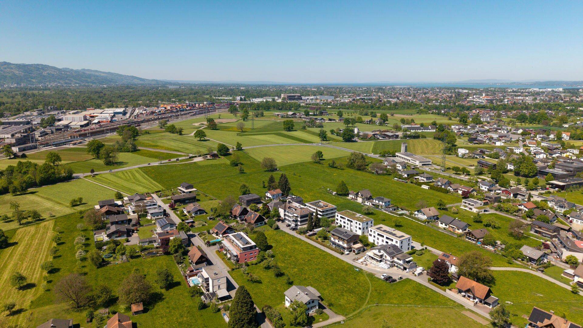 Luftaufnahme einer ländlichen Wohnsiedlung mit weiten Feldern und einem Industriegebiet am Horizont.