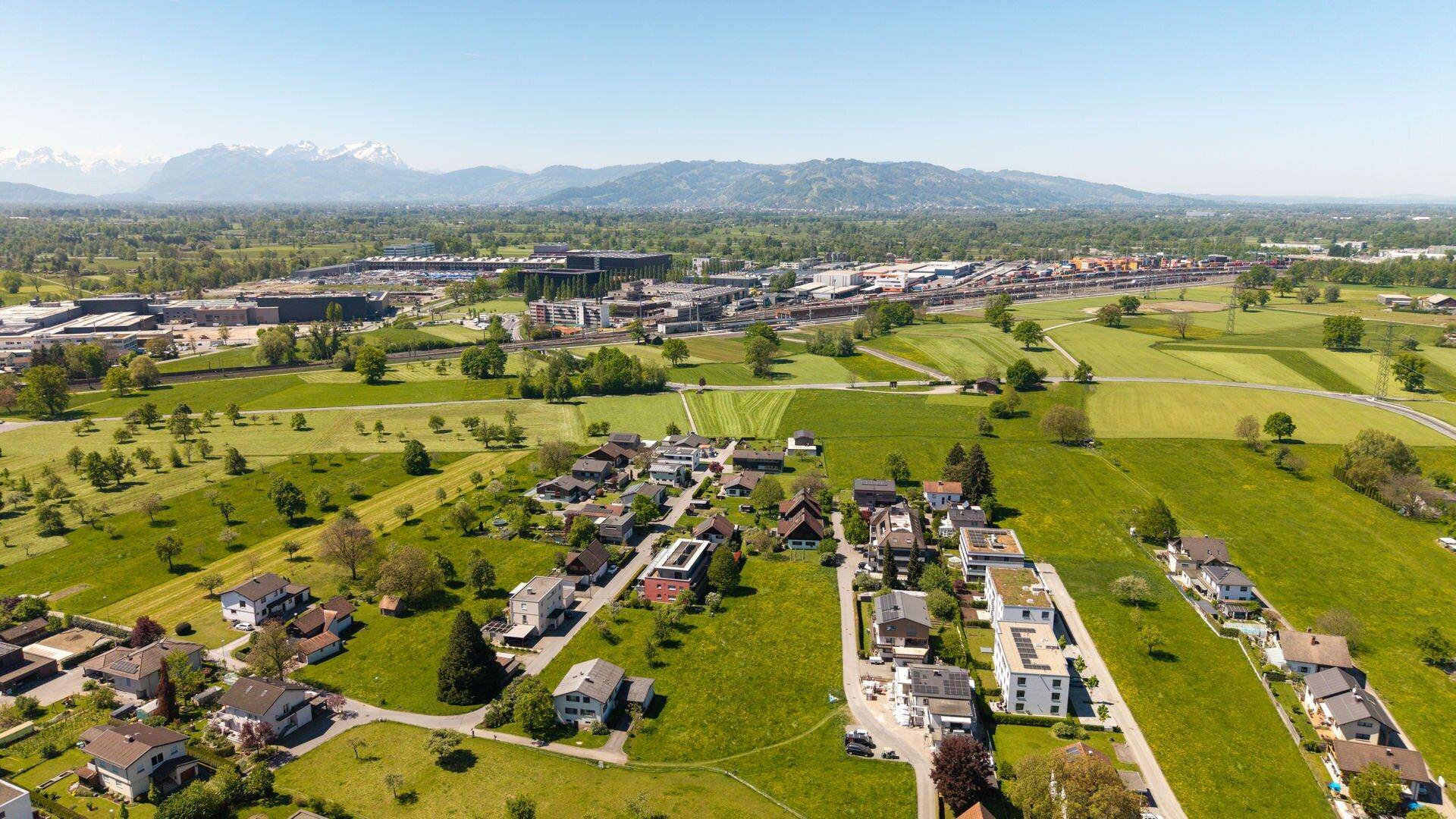 Weitwinkel-Luftaufnahme einer Wohngegend mit grünen Feldern und schneebedeckten Bergen am Horizont.