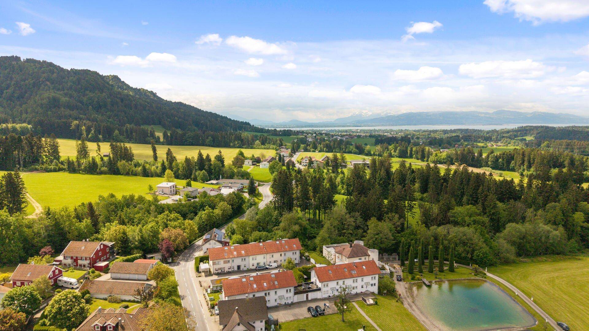 Panoramablick auf eine ländliche Siedlung mit weiten Feldern und einem See in der Ferne.