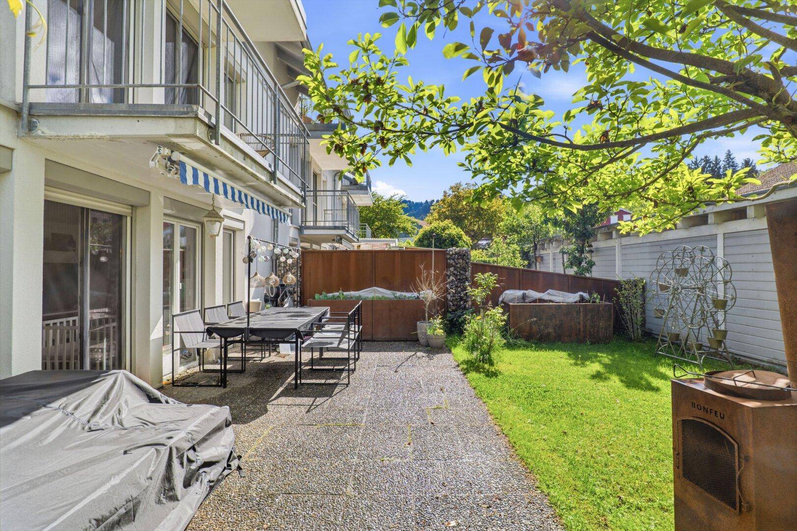 Terrasse mit Gartenmöbeln, Rasenfläche und Blick auf das Gebäude.