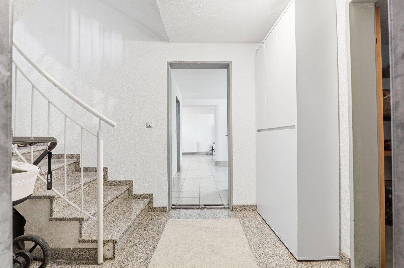 Heller Flur im Untergeschoss mit Treppe und Fliesenboden.