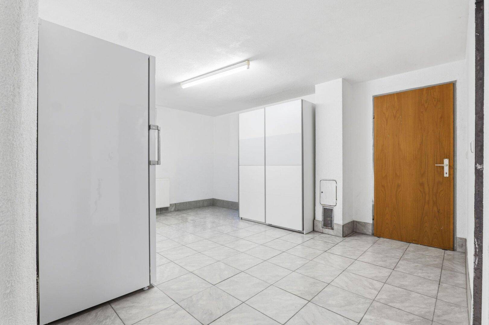 Heller Kellerraum mit Fliesenboden und weißem Schrank.